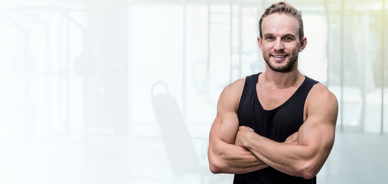 Smiling athletic man in a black tank top with his arms crossed in a gym